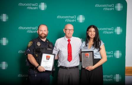 是以年代. Ali, MD, and Officer Eric Hunter hold awards and stand on either side of Terry Dion.